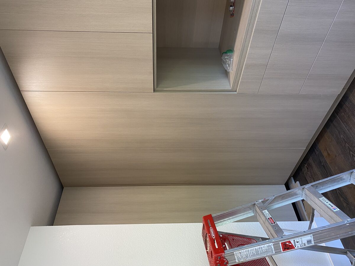 Floor-to-ceiling custom closet by DodiHome with light oak laminate finish, open display niche, and integrated drawers