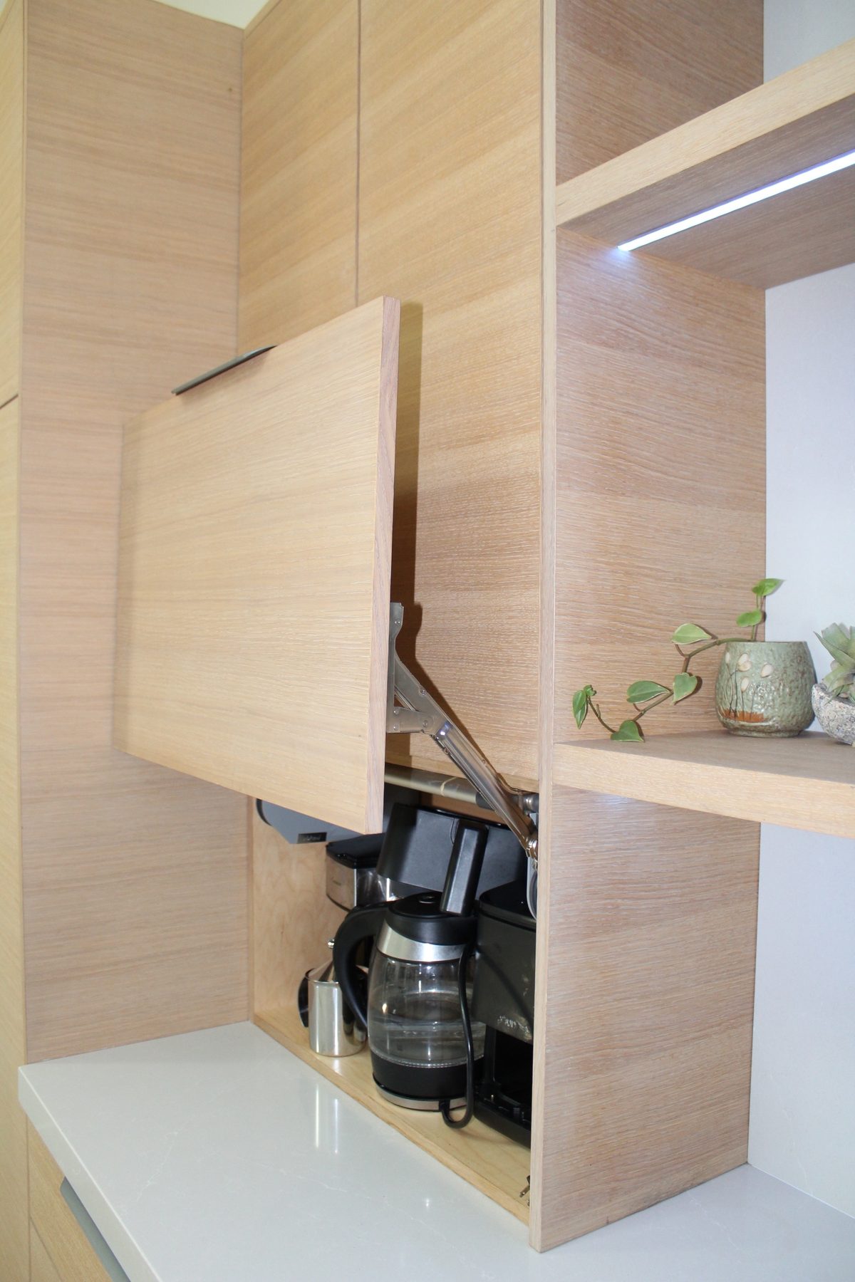 Flip-up appliance garage door open above a concealed coffee and kettle station in the oak kitchen