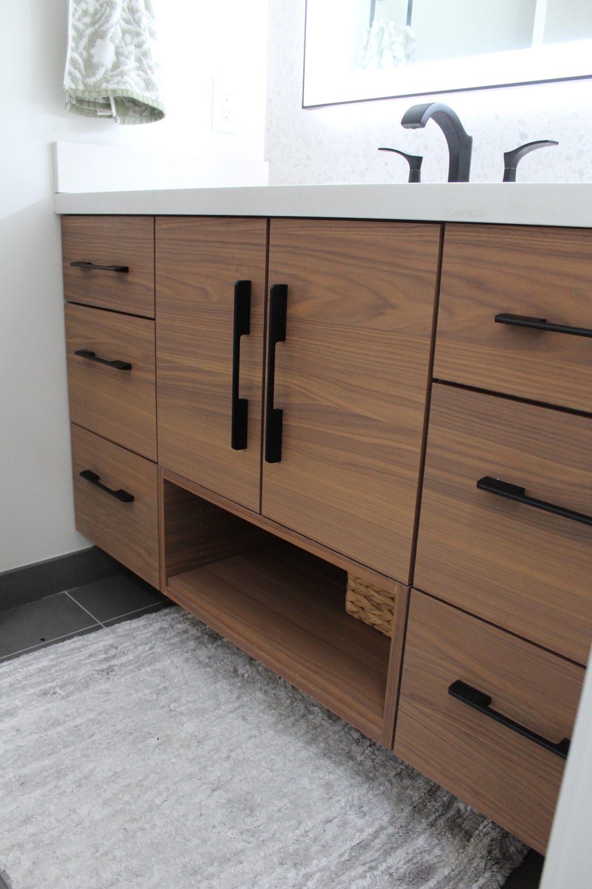 Symmetric walnut bathroom vanity with drawer banks flanking a double-door cabinet and open cubby