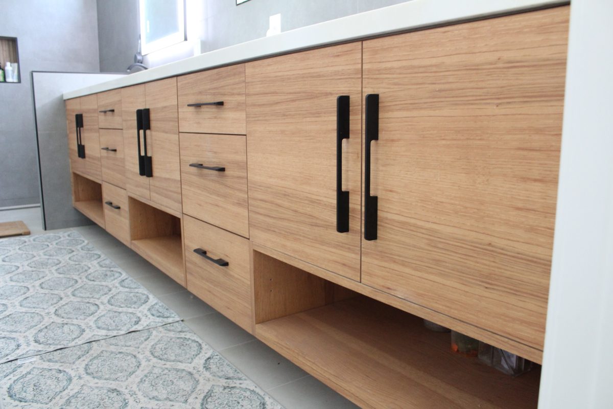 Straight-on view of the light oak vanity run with backlit mirrors and large-format gray tile