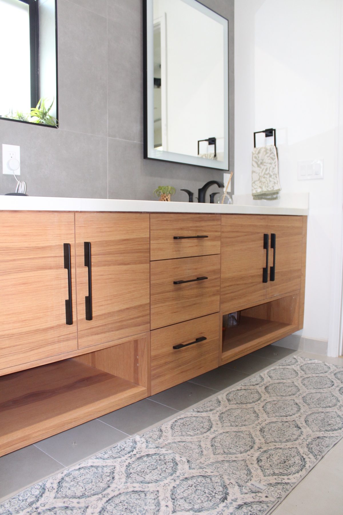 Styled vanity vignette with folded towel, succulent, and black faucet against gray tile