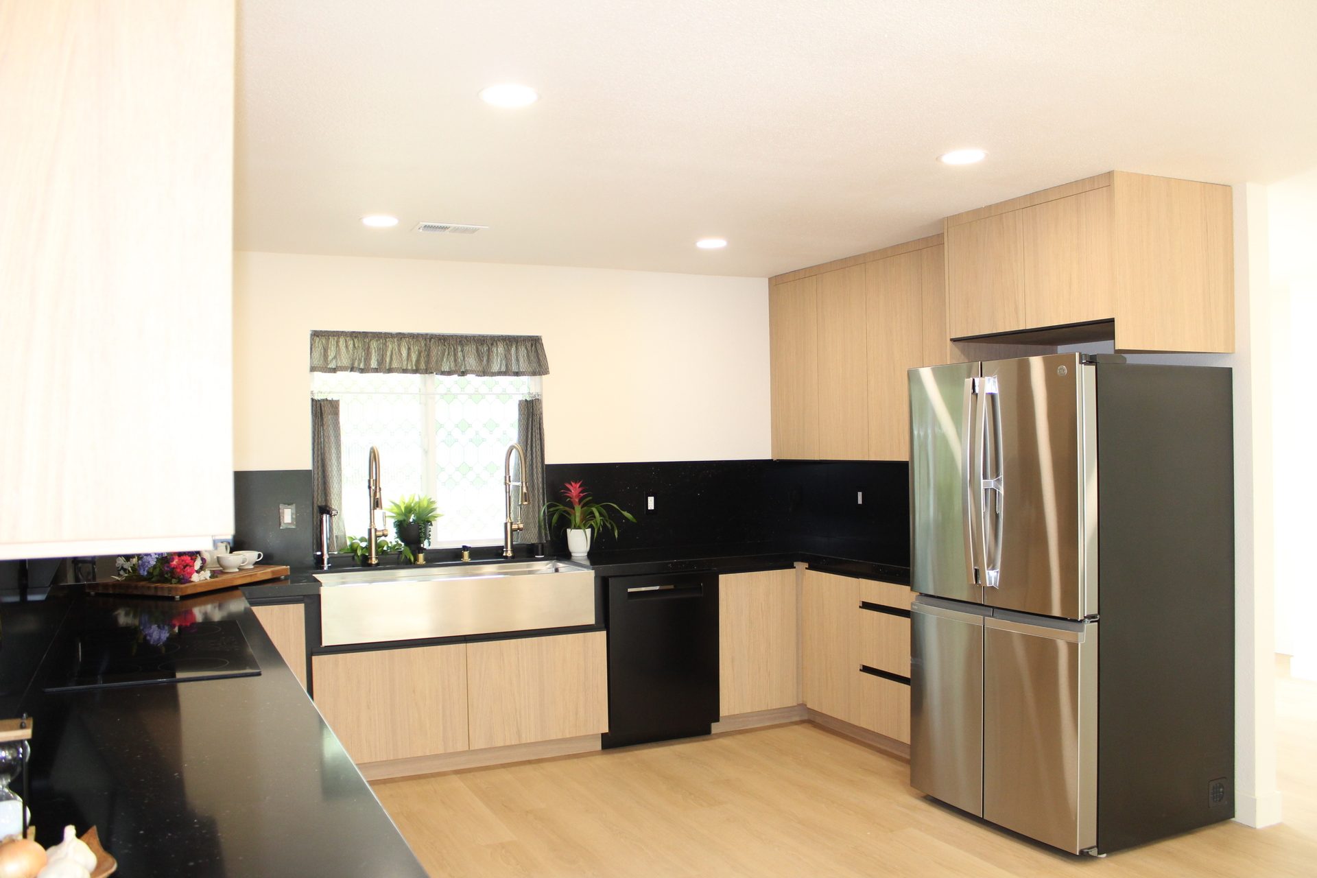 Full view of a U-shaped light oak kitchen with black quartz counters, stainless farmhouse sink, and integrated range hood