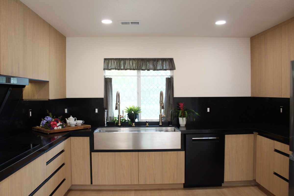 Wide view of the kitchen from the opposite end showing tall oak cabinetry and dual brass faucets over the farmhouse sink