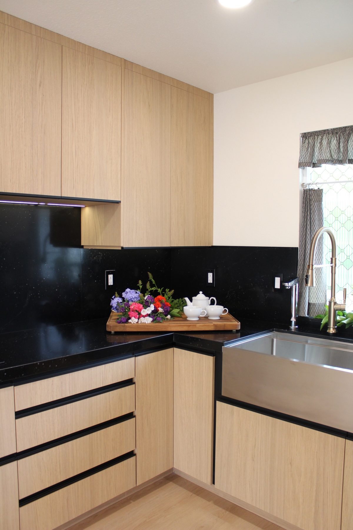 Vertical view of the counter corner where black quartz surfaces meet light oak base and tall cabinets