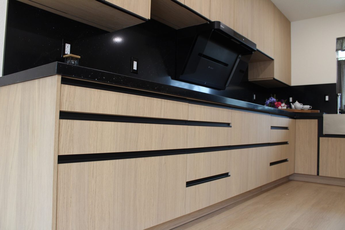 Range hood and countertop vignette with light oak uppers and black quartz backsplash detail