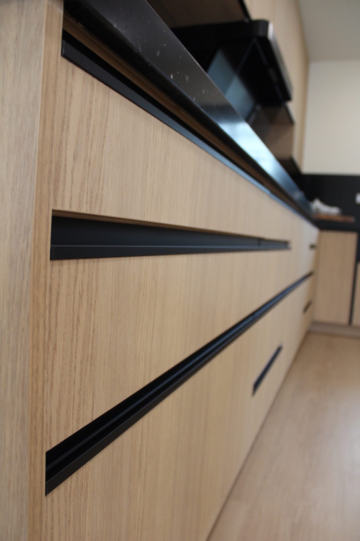 Close-up of recessed black finger-pull channels routed into light oak drawer fronts