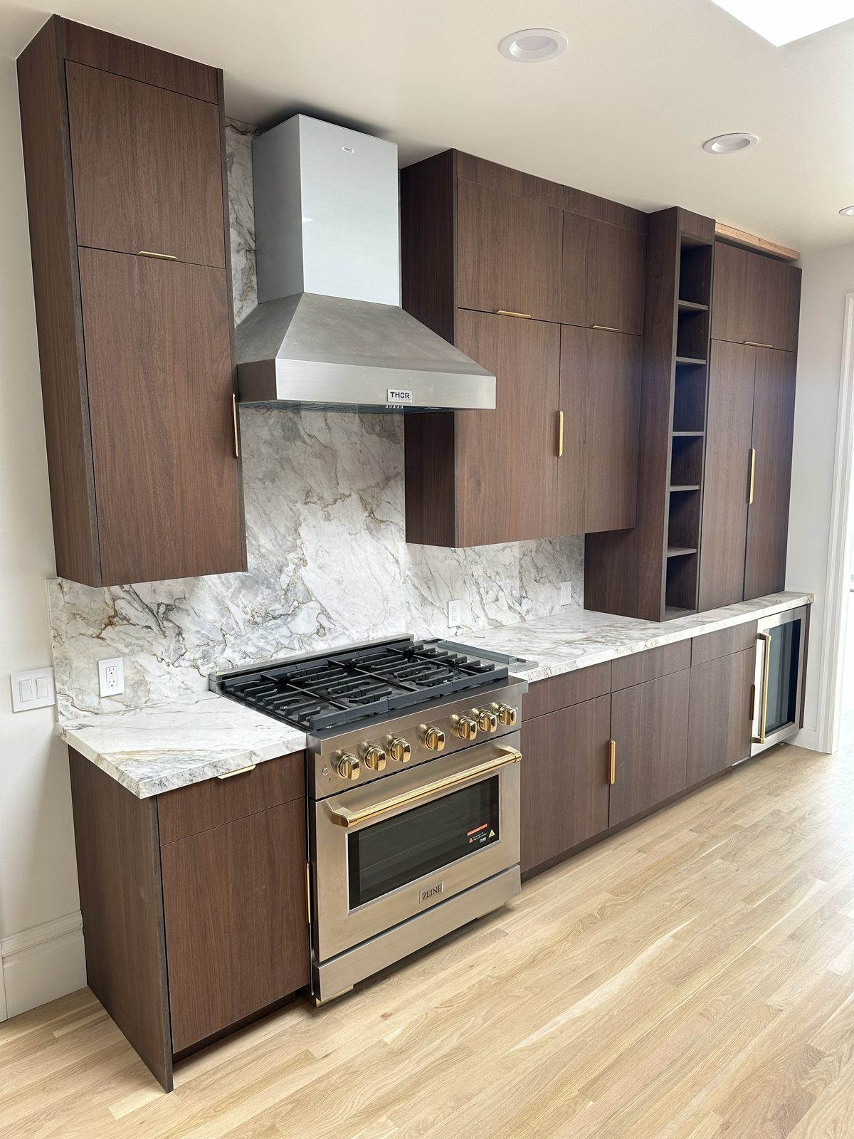 Walnut cabinet wall with integrated range, hood, and wine fridge under warm lighting