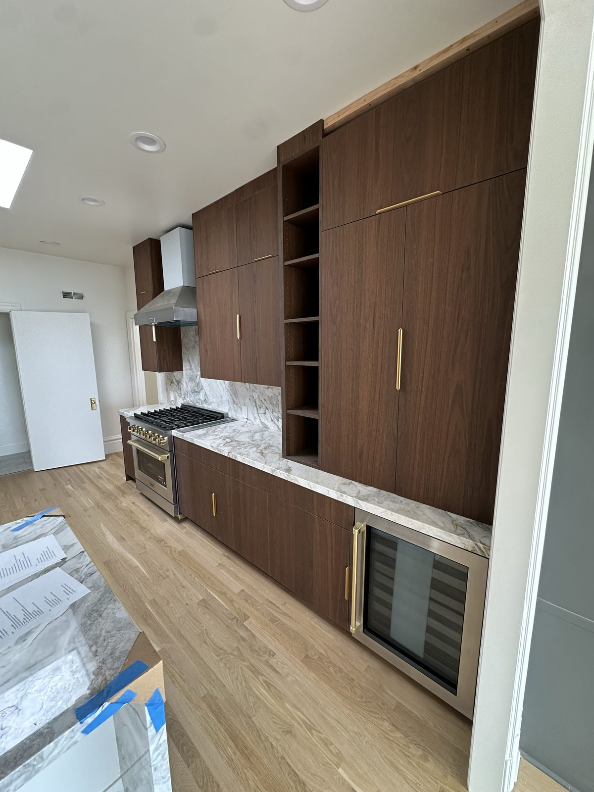 Wide view of the walnut slab kitchen with marble waterfall island and brass hardware