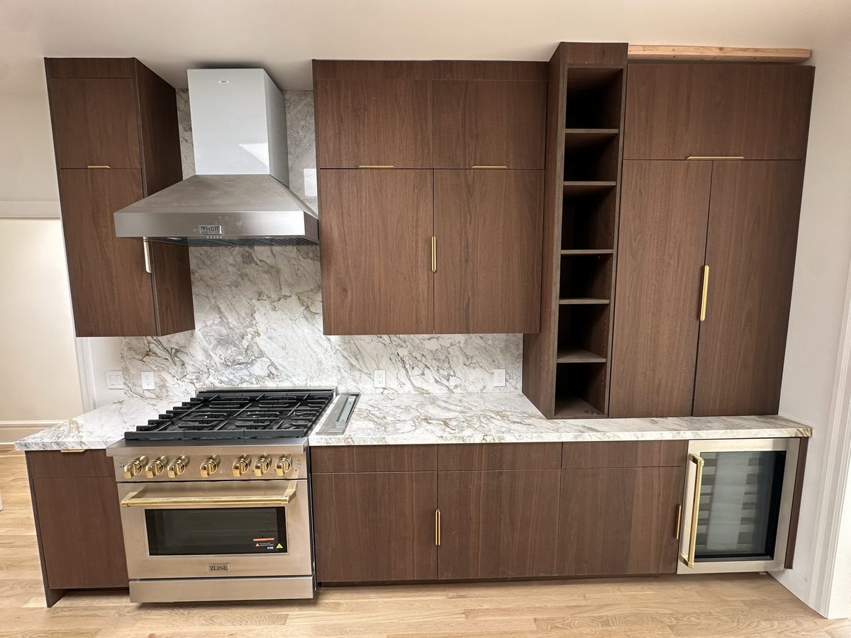 Angled view of the walnut kitchen run showing the marble island edge and pantry tower