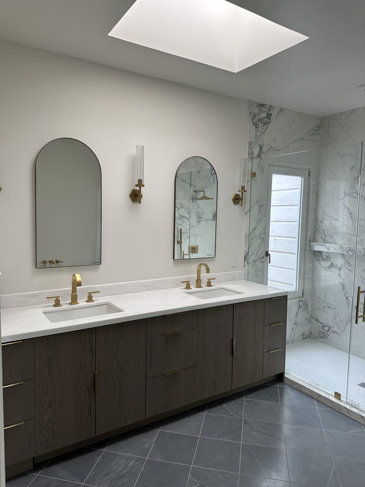 Second angle of the primary bath vanity showing arched black mirrors and marble shower glass