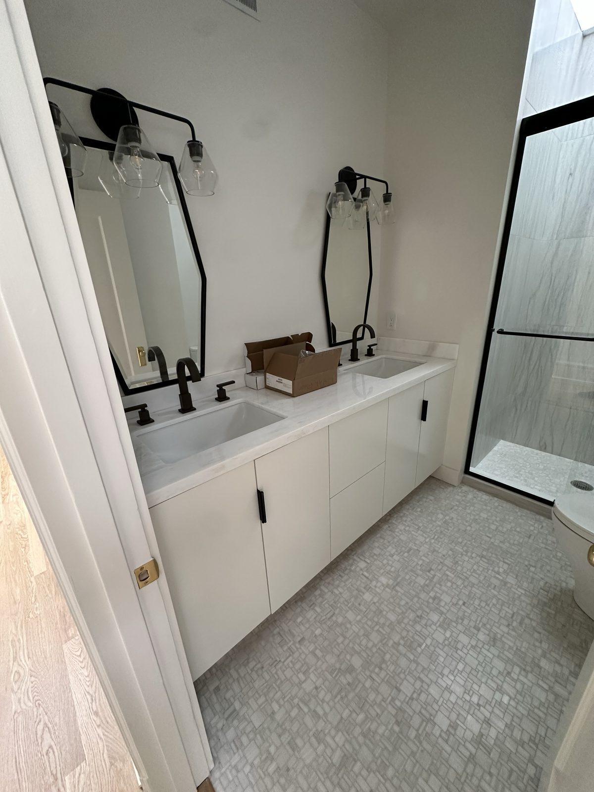 White hallway bathroom double vanity with black hardware and mosaic tile floor